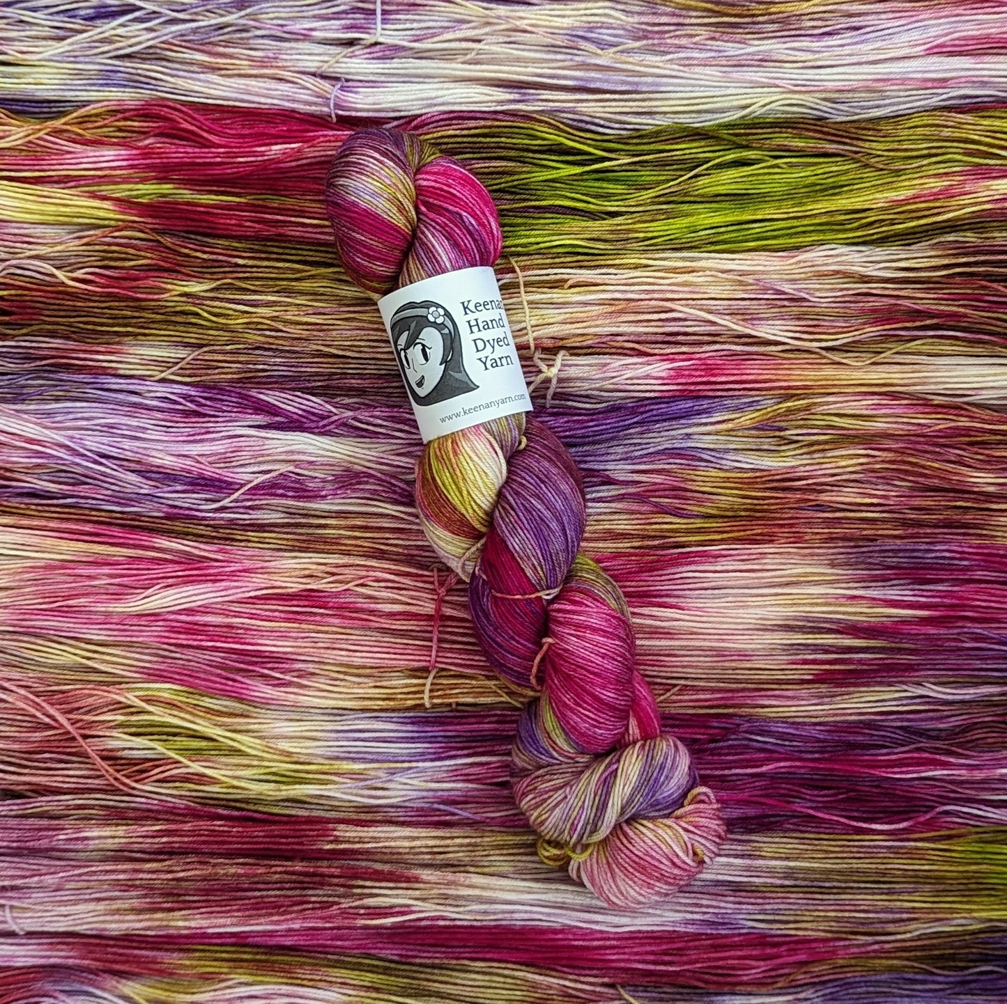 A skein of violet, magenta, and lime green sock yarn on a field of the same yarn laid underneath it